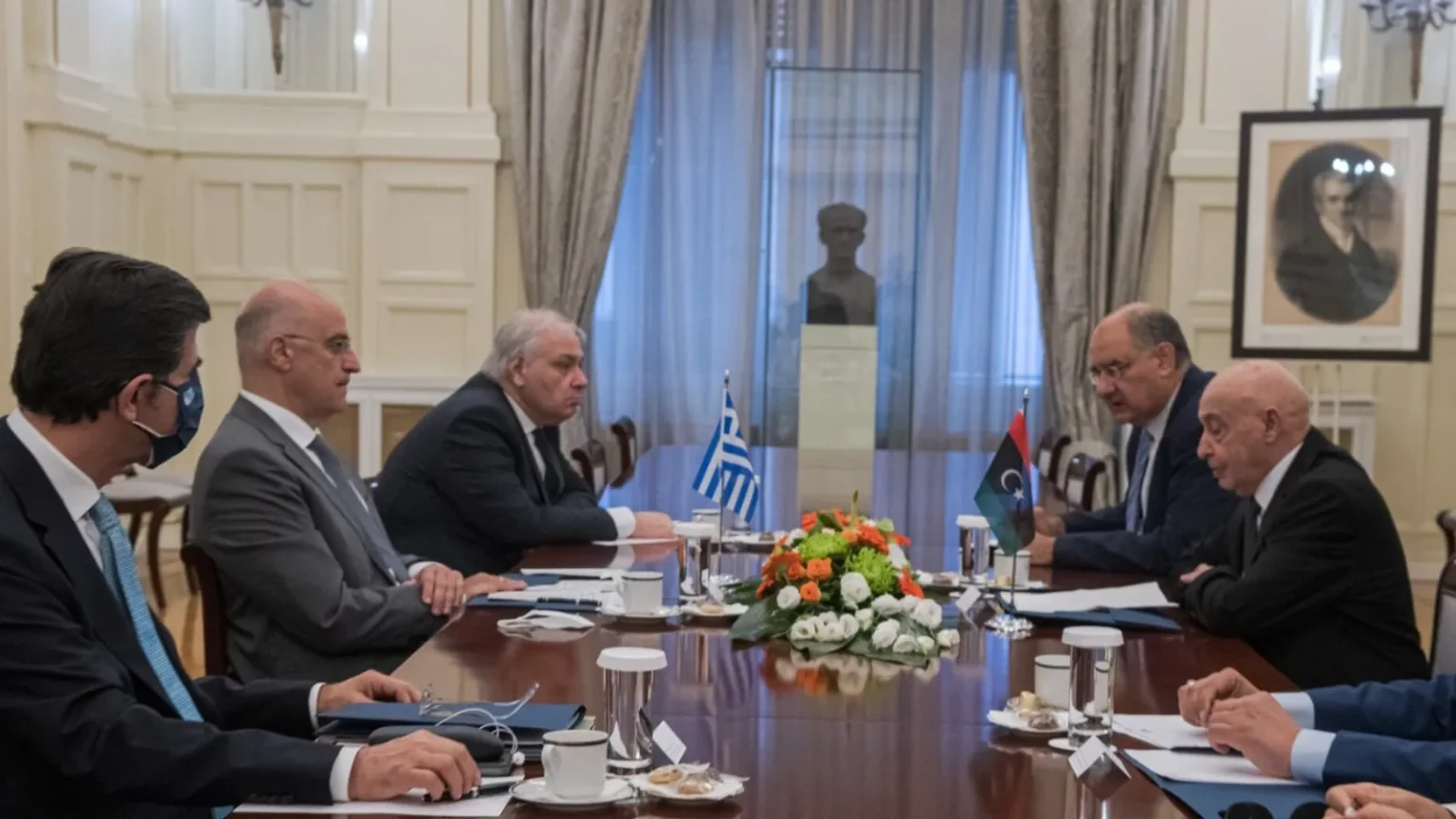 Ο Αγκίλα Σάλεχ και η λιβυκή αντιπροσωπεία απέναντι από την ελληνική αντιπροσωπεία με τον Νίκο Δένδια, με ελληνική και λιβυκή σημαία στο τραπέζι