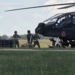 Επιθετικό ελικόπτερο AH-64E Apache σταθμευμένο σε χορτολιβαδική έκταση, με στρατιώτες να το προετοιμάζουν