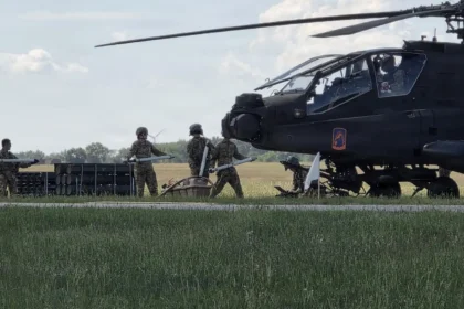 Επιθετικό ελικόπτερο AH-64E Apache σταθμευμένο σε χορτολιβαδική έκταση, με στρατιώτες να το προετοιμάζουν