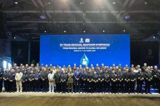 Αρχηγοί ναυτικών και σύνεδροι σε ομαδική φωτογραφία μπροστά σε οθόνη με τίτλο XV Trans-Regional Seapower Symposium