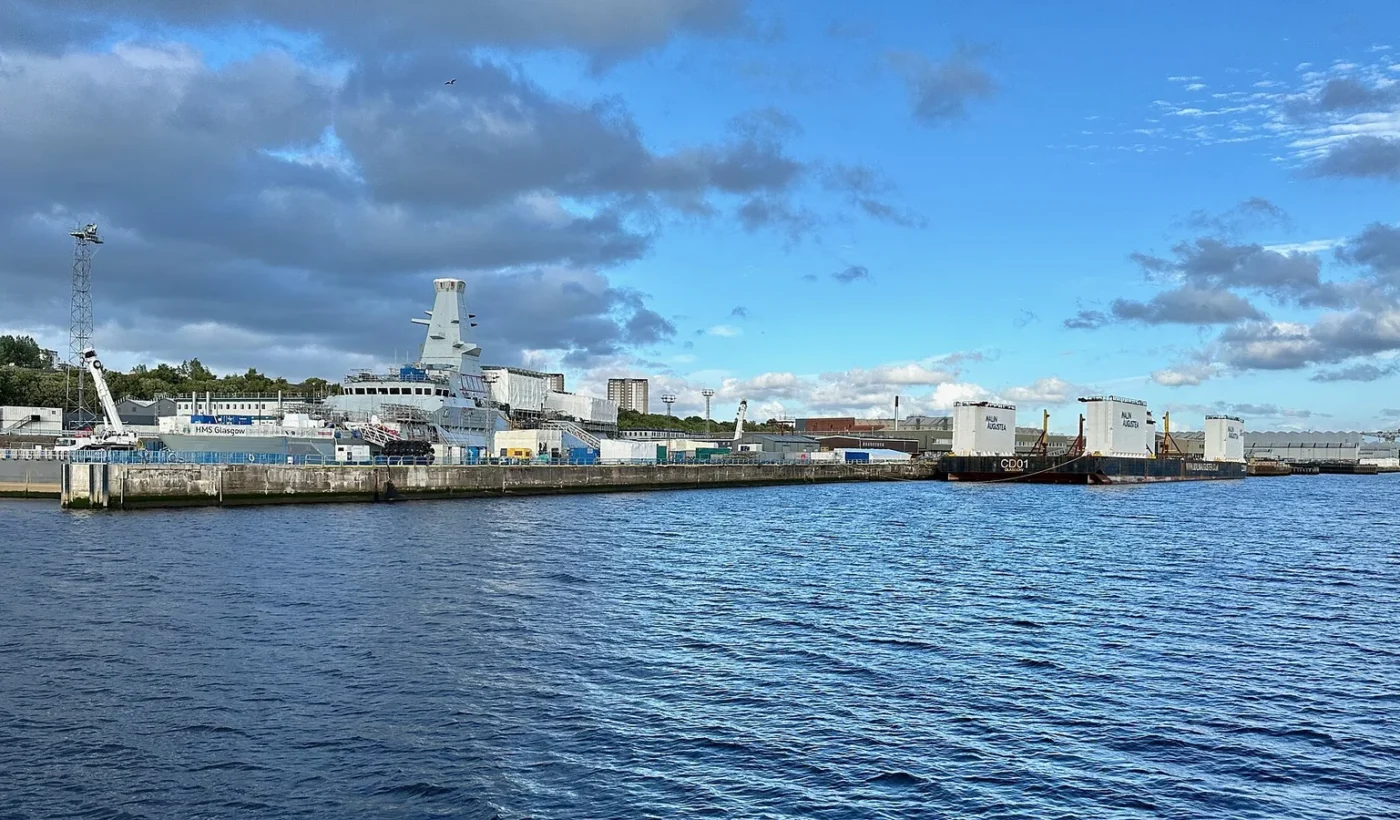 Η φρεγάτα Type 26 HMS Glasgow δεμένη στην αποβάθρα του ναυπηγείου Σκότστουν στον ποταμό Κλάιντ, με μια πλωτή φορτηγίδα στα δεξιά