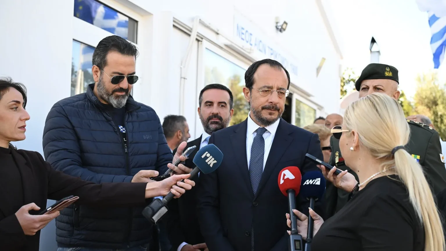 Ο Πρόεδρος της Κυπριακής Δημοκρατίας Νίκος Χριστοδουλίδης με σκούρο κοστούμι μιλά σε δημοσιογράφους που κρατούν μικρόφωνα