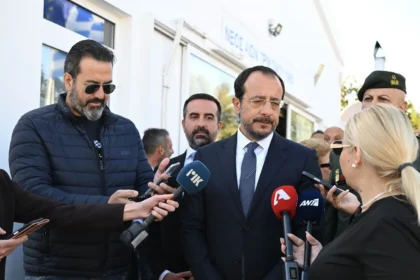 Ο Πρόεδρος της Κυπριακής Δημοκρατίας Νίκος Χριστοδουλίδης με σκούρο κοστούμι μιλά σε δημοσιογράφους που κρατούν μικρόφωνα