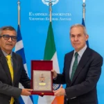 Ο Θανάσης Δαβάκης και ο Ρατζές Κουμάρ Σινγκ κρατούν αναμνηστική πλακέτα μπροστά από τις σημαίες Ελλάδας και Ινδίας