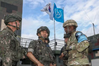 Αξιωματικοί της Νότιας Κορέας και των ΗΠΑ με κράνη συνομιλούν σε φυλάκιο, με τις σημαίες της Νότιας Κορέας και του ΟΗΕ στο βάθος