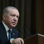 Ο Ρετζέπ Ταγίπ Ερντογάν μιλά σε βήμα με μικρόφωνα σε σκοτεινή αίθουσα