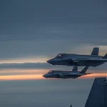 Δύο φινλανδικά F-35A πετούν σε σχηματισμό στο σούρουπο, με την ουρά ενός F/A-18 Hornet σε πρώτο πλάνο