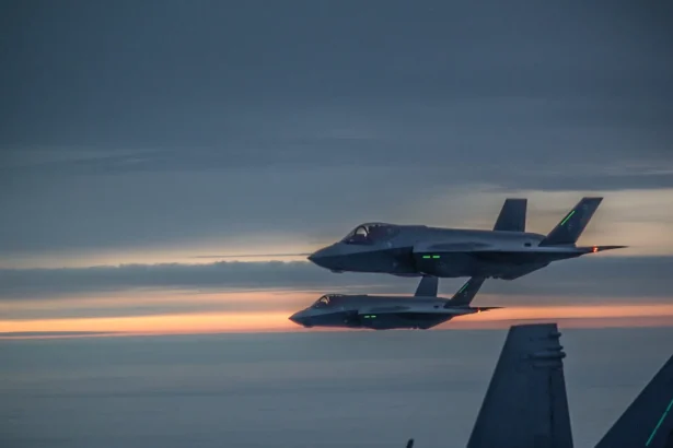 Δύο φινλανδικά F-35A πετούν σε σχηματισμό στο σούρουπο, με την ουρά ενός F/A-18 Hornet σε πρώτο πλάνο