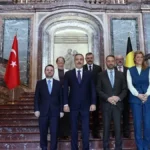 Ο Χακάν Φιντάν με Τούρκους και Βέλγους υπουργούς σε μαρμάρινη σκάλα ανάμεσα σε τουρκικές και βελγικές σημαίες