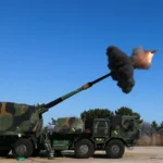 Τροχοφόρο αυτοκινούμενο πυροβόλο με παραλλαγή ρίχνει βολή, με καπνό στο στόμιο της κάνης και το βλήμα στον αέρα