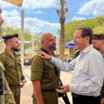 Ο Ισραηλινός πρόεδρος με λευκό πουκάμισο αγκαλιάζει στρατιώτη ανάμεσα σε στρατιώτες με χακί στολές σε στρατόπεδο