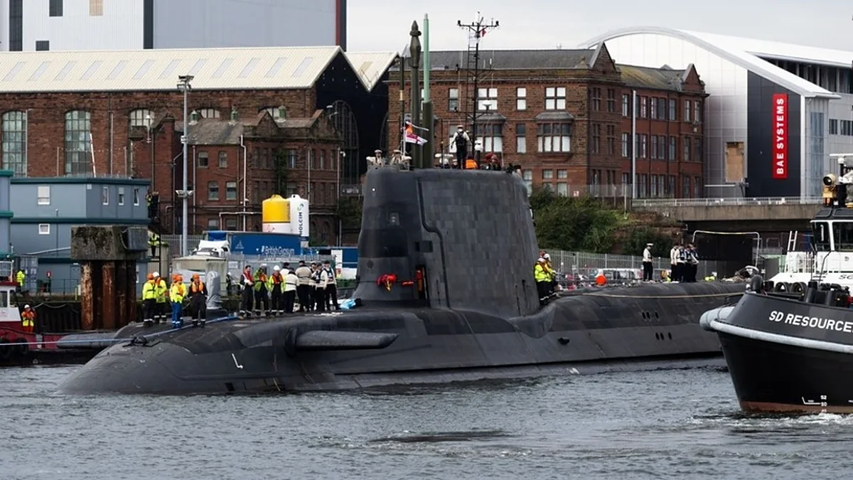 Το πυρηνοκίνητο υποβρύχιο HMS Agamemnon κλάσης Astute στο λιμάνι του Μπάροου-ιν-Φέρνες, με μέλη του πληρώματος στο κατάστρωμα και ρυμουλκό δίπλα του