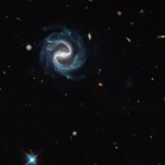 Εικόνα του Hubble με σπειροειδή γαλαξία με ράβδο στο κέντρο και βαρυτικό φακό στην κάτω δεξιά γωνία