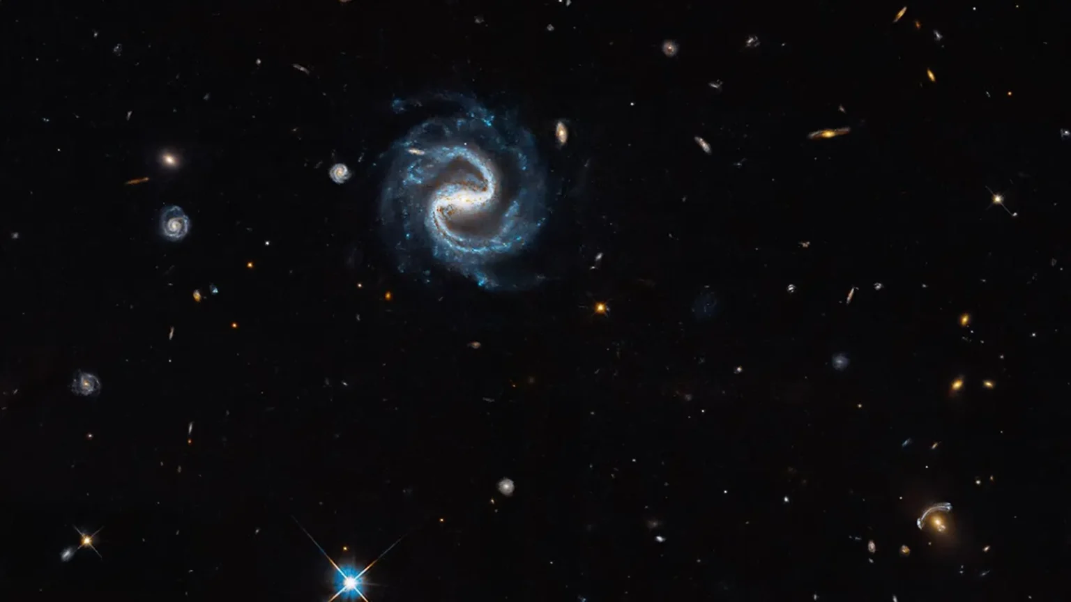 Εικόνα του Hubble με σπειροειδή γαλαξία με ράβδο στο κέντρο και βαρυτικό φακό στην κάτω δεξιά γωνία