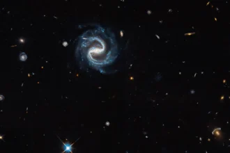 Εικόνα του Hubble με σπειροειδή γαλαξία με ράβδο στο κέντρο και βαρυτικό φακό στην κάτω δεξιά γωνία