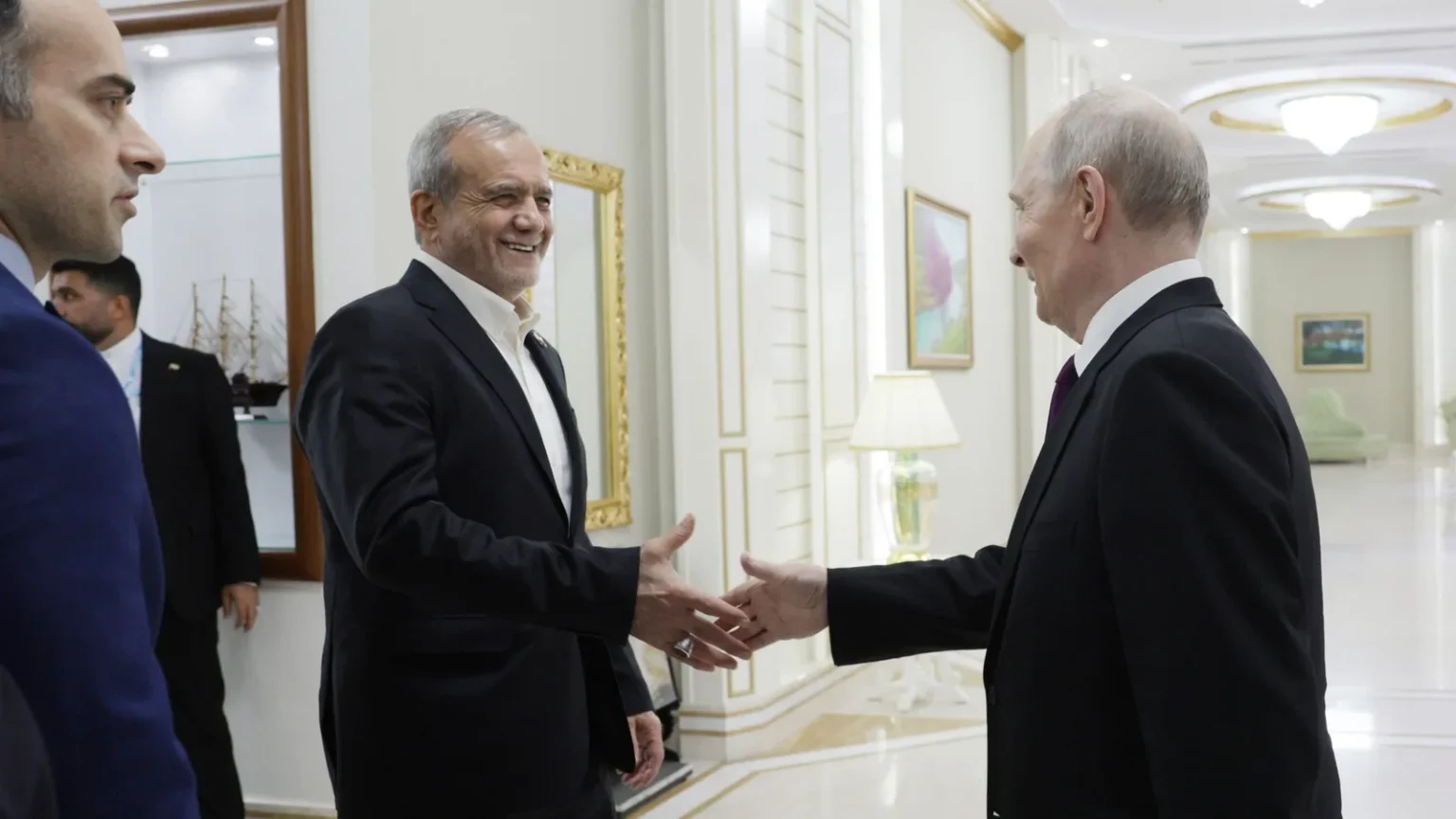 Ο Ιρανός πρόεδρος Μασούντ Πεζεσκιάν χαμογελά καθώς χαιρετά τον Βλαντιμίρ Πούτιν σε διάδρομο κτιρίου