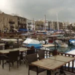 Τραπεζάκια καφέ, σκάφη και πέτρινα κτίρια στο παλιό λιμάνι της Κερύνειας
