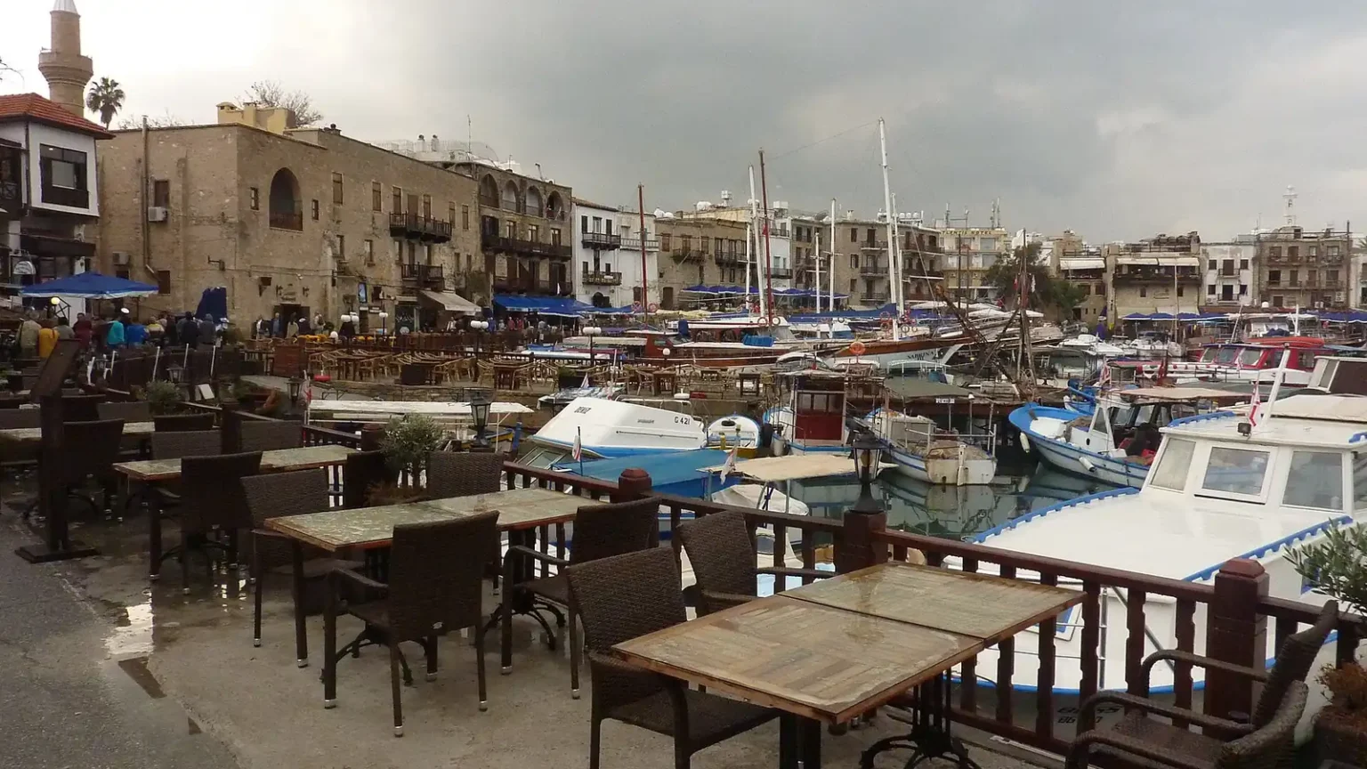 Τραπεζάκια καφέ, σκάφη και πέτρινα κτίρια στο παλιό λιμάνι της Κερύνειας