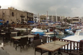 Τραπεζάκια καφέ, σκάφη και πέτρινα κτίρια στο παλιό λιμάνι της Κερύνειας