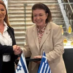 Η υπουργός Πολιτισμού Λίνα Μενδώνη και η πρέσβης του Ισραήλ Pninat Yanay σφίγγουν τα χέρια πίσω από τραπέζι με ισραηλινή και ελληνική σημαία στο Εθνικό Αρχαιολογικό Μουσείο