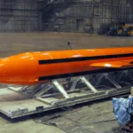 Πορτοκαλί βόμβα GBU-43/B MOAB πάνω σε μεταλλική βάση μεταφοράς μέσα σε υπόστεγο