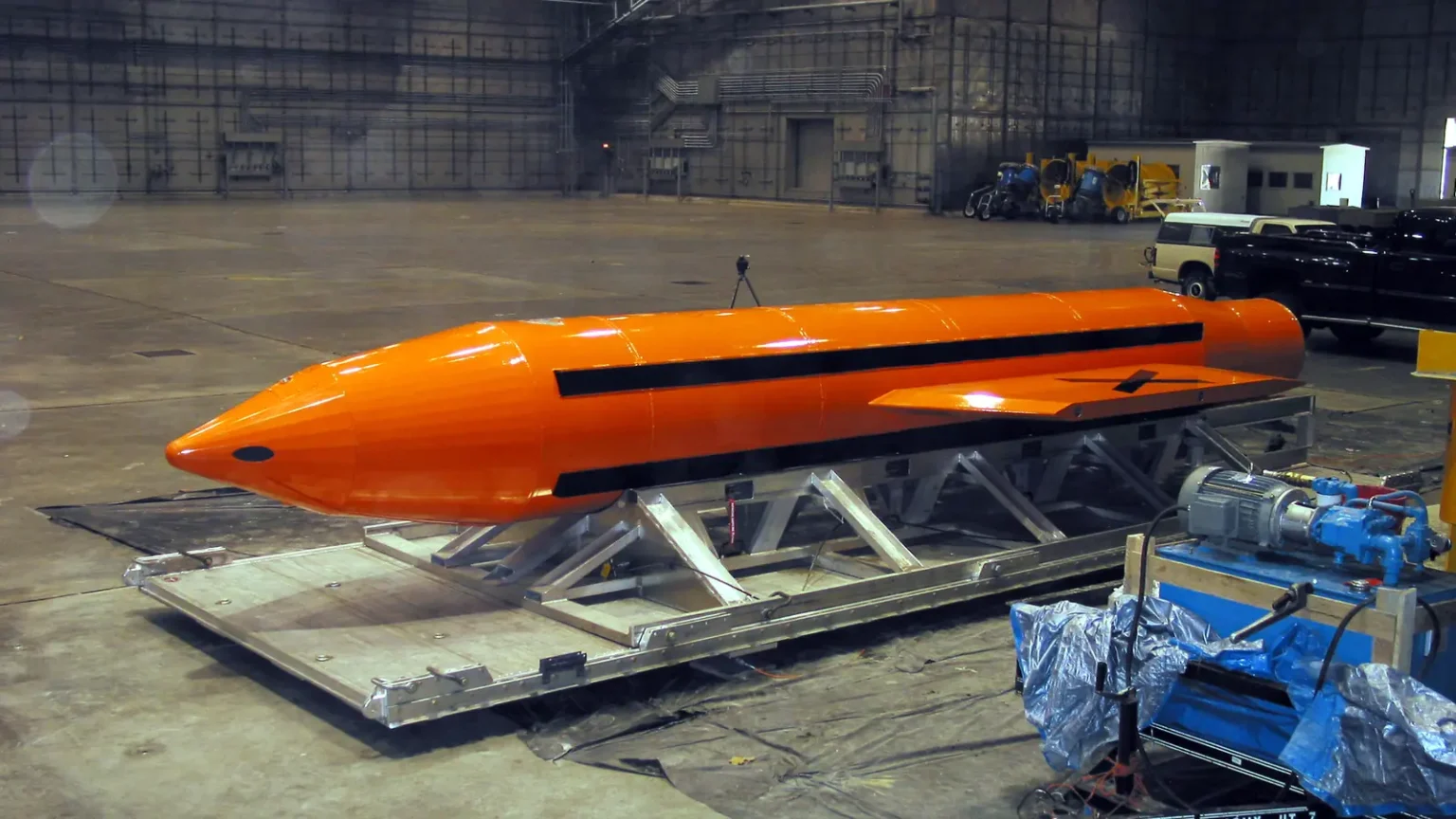 Πορτοκαλί βόμβα GBU-43/B MOAB πάνω σε μεταλλική βάση μεταφοράς μέσα σε υπόστεγο