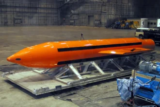 Πορτοκαλί βόμβα GBU-43/B MOAB πάνω σε μεταλλική βάση μεταφοράς μέσα σε υπόστεγο