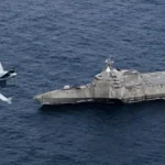 Μη επανδρωμένο αεροσκάφος MQ-9B SeaGuardian πετά χαμηλά πάνω από τη θάλασσα δίπλα στο πλοίο USS Coronado