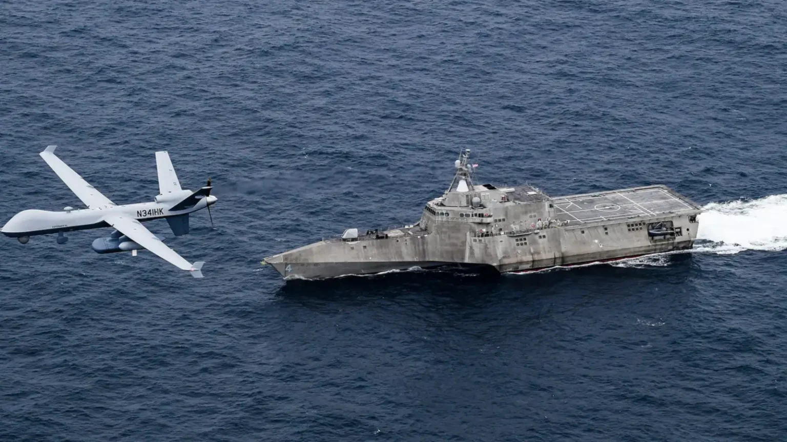 Μη επανδρωμένο αεροσκάφος MQ-9B SeaGuardian πετά χαμηλά πάνω από τη θάλασσα δίπλα στο πλοίο USS Coronado