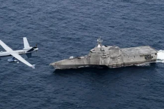 Μη επανδρωμένο αεροσκάφος MQ-9B SeaGuardian πετά χαμηλά πάνω από τη θάλασσα δίπλα στο πλοίο USS Coronado