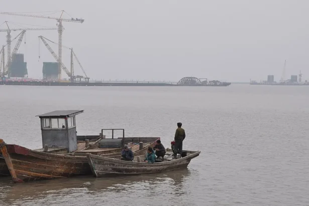 Γερανοί και πυλώνες της υπό κατασκευή γέφυρας στον ποταμό Γιαλού, με ψαρόβαρκες σε πρώτο πλάνο