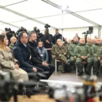 Στρατιωτικοί και πολιτικοί κάθονται σε σκηνή ενημέρωσης, με drones εκτεθειμένα σε πρώτο πλάνο, στην άσκηση Blue Eye-26