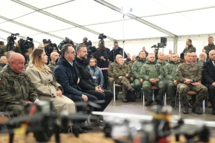 Στρατιωτικοί και πολιτικοί κάθονται σε σκηνή ενημέρωσης, με drones εκτεθειμένα σε πρώτο πλάνο, στην άσκηση Blue Eye-26