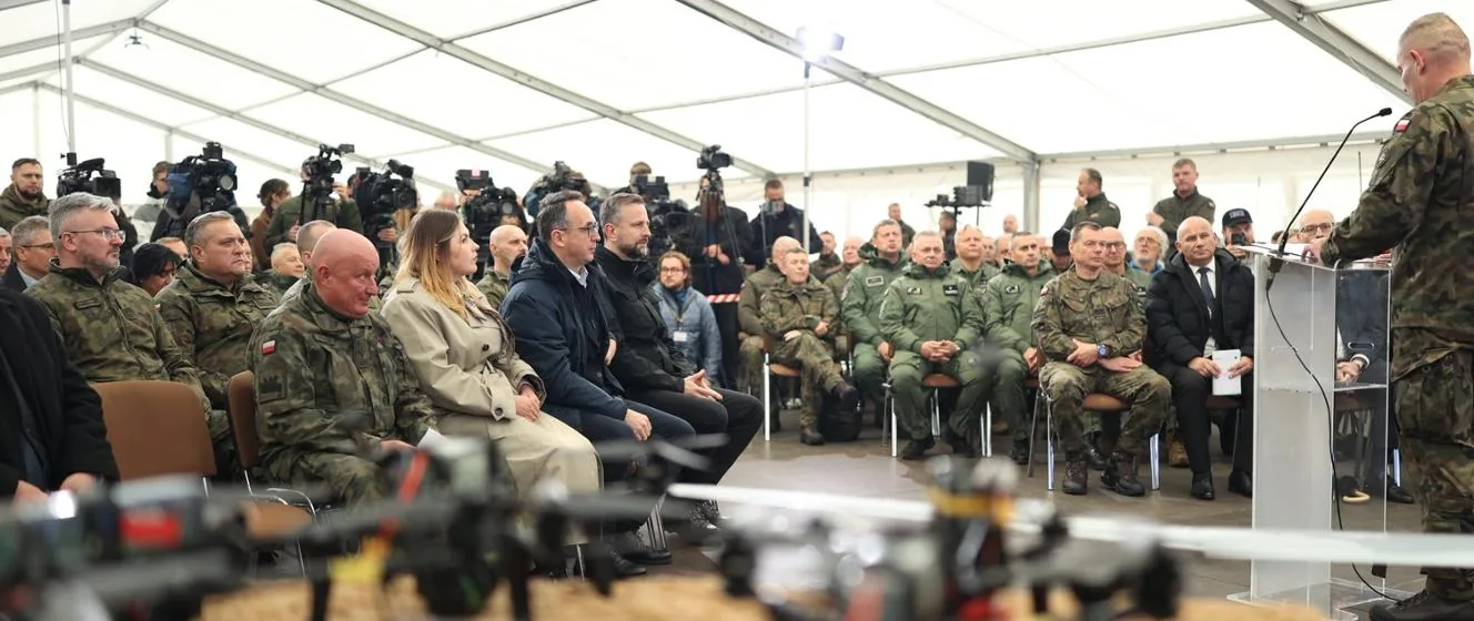 Στρατιωτικοί και πολιτικοί κάθονται σε σκηνή ενημέρωσης, με drones εκτεθειμένα σε πρώτο πλάνο, στην άσκηση Blue Eye-26