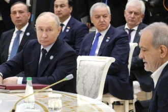 Ο Βλαντίμιρ Πούτιν καθισμένος σε τραπέζι συνεδρίασης, με τον Μασούντ Πεζεσκιάν στα δεξιά και αντιπροσωπείες πίσω τους