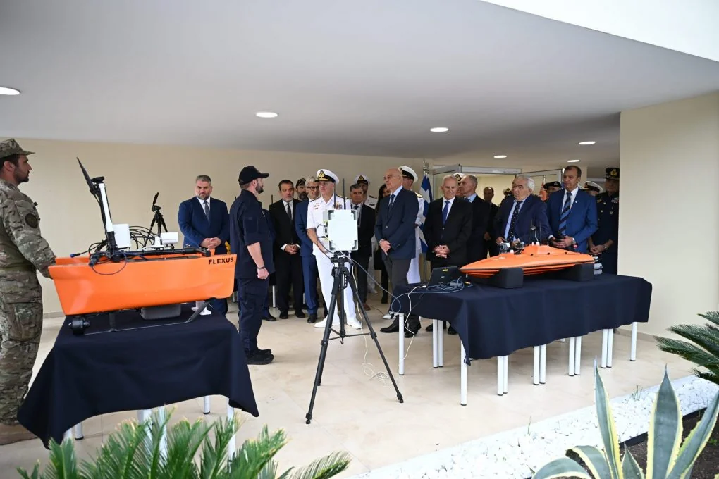Ο Νίκος Δένδιας και αξιωματικοί παρακολουθούν παρουσίαση μικρών πορτοκαλί μη επανδρωμένων σκαφών πάνω σε τραπέζια