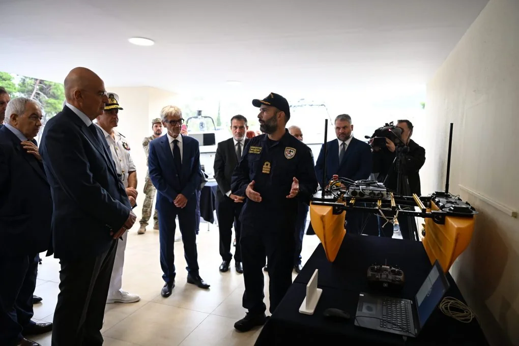 Αξιωματικός εξηγεί στον Νίκο Δένδια τη λειτουργία μικρού κίτρινου σκάφους δύο γαστρών με κεραίες, δίπλα σε φορητό υπολογιστή και χειριστήριο