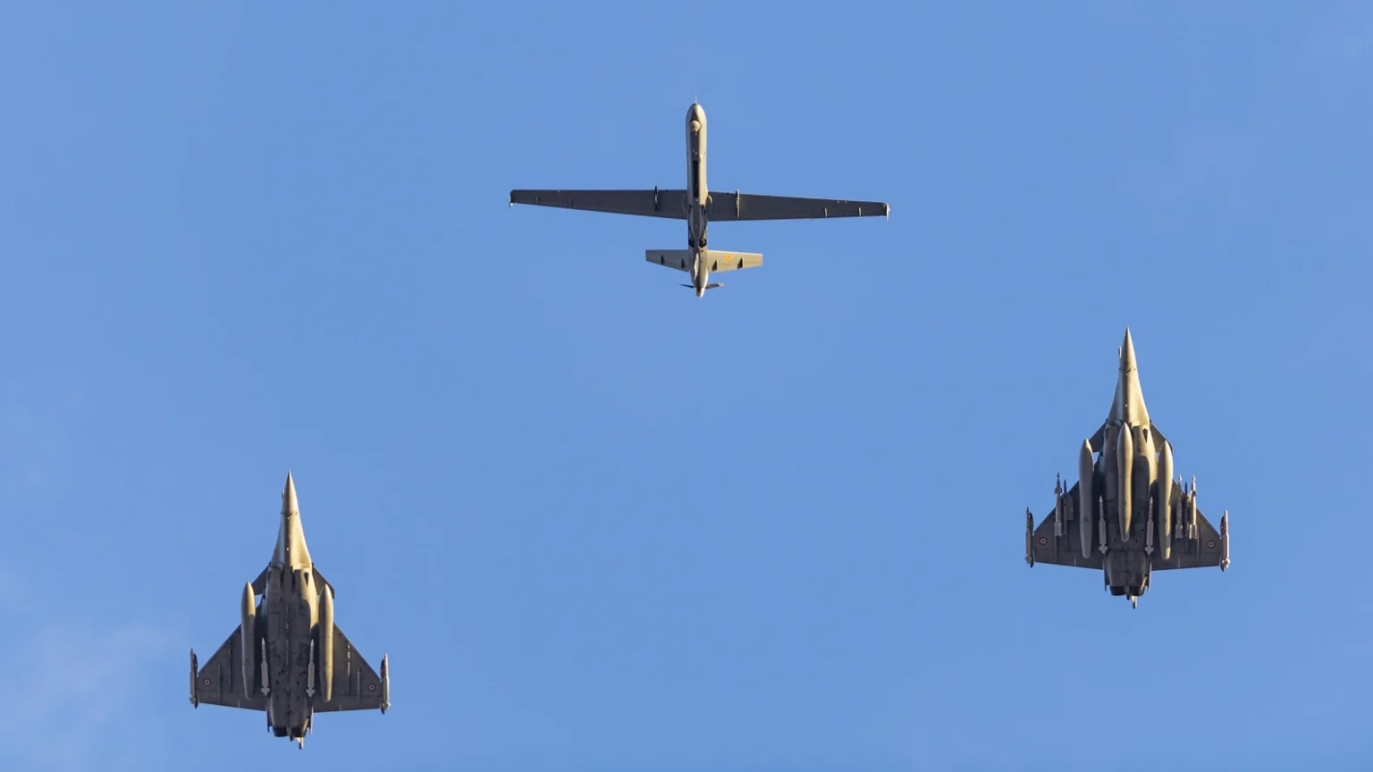 Δύο μαχητικά Rafale και ένα μη επανδρωμένο αερόχημα Reaper πετούν σε σχηματισμό, φωτογραφημένα από το έδαφος