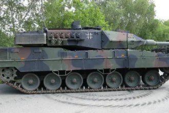 Πλάγια όψη άρματος μάχης Leopard 2A7 με παραλλαγή σε άσφαλτο, με δέντρα στο φόντο