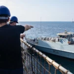 Βρετανοί ναυτικοί στο κατάστρωμα του RFA Lyme Bay δείχνουν το ναρκοθηρευτικό HMS Penzance (M106) που πλέει δίπλα τους στον Κόλπο του Ομάν