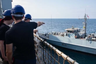 Βρετανοί ναυτικοί στο κατάστρωμα του RFA Lyme Bay δείχνουν το ναρκοθηρευτικό HMS Penzance (M106) που πλέει δίπλα τους στον Κόλπο του Ομάν