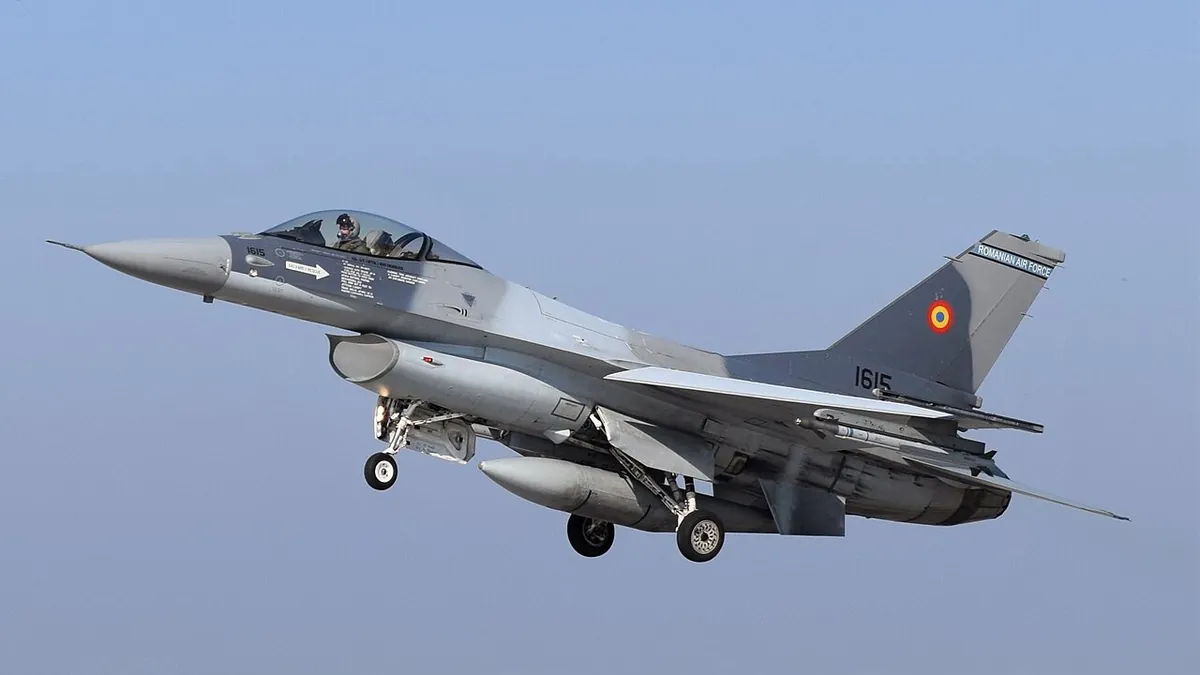 Γκρι μαχητικό F-16 με το ρουμανικό σήμα στο κάθετο σταθερό, σε πτήση με κατεβασμένα σκέλη προσγείωσης