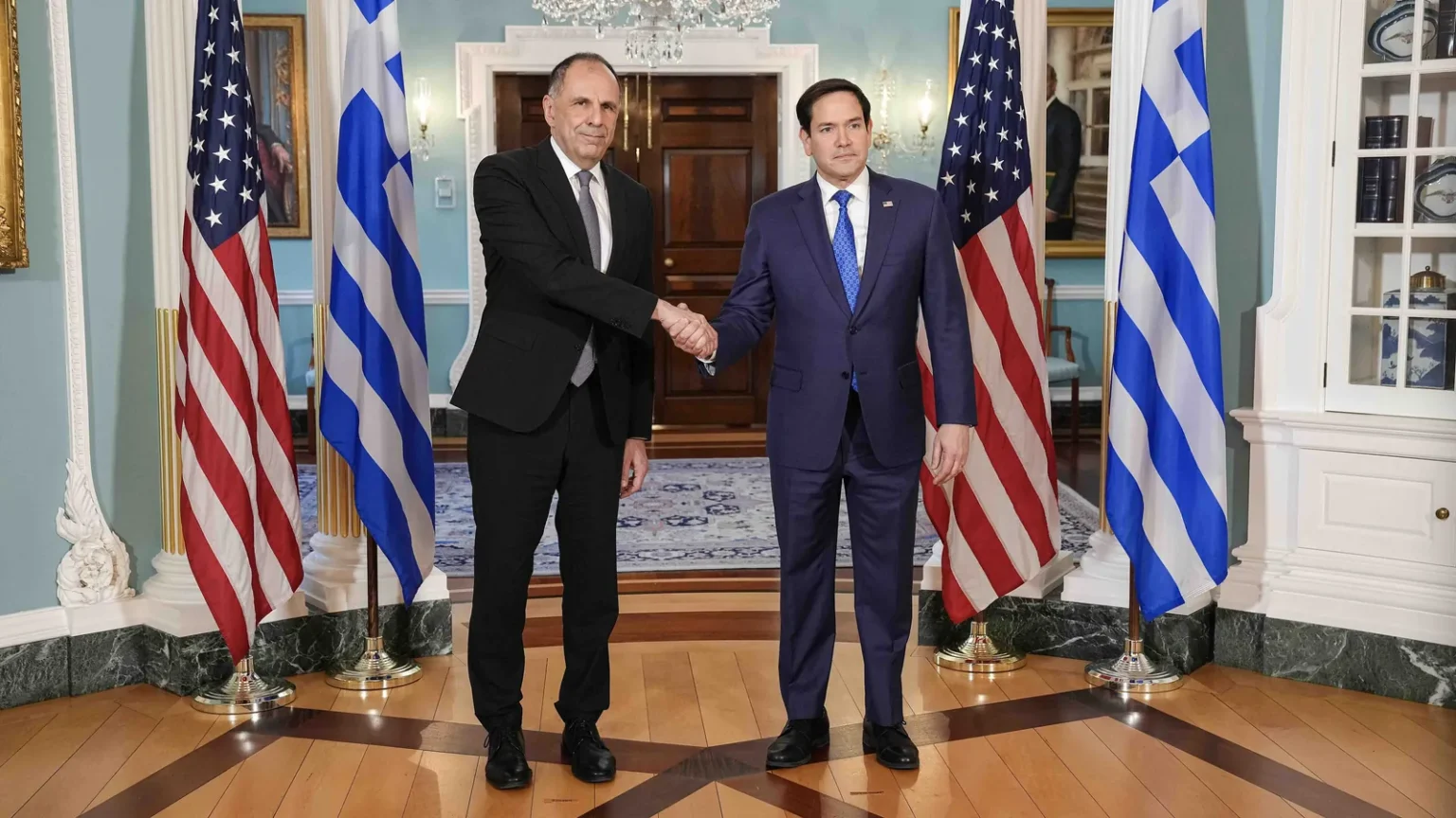 Ο Γιώργος Γεραπετρίτης και ο Μάρκο Ρούμπιο ανταλλάσσουν χειραψία μπροστά σε ελληνικές και αμερικανικές σημαίες στο Στέιτ Ντιπάρτμεντ