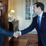 Ο Σαντάμ Χαφτάρ σφίγγει το χέρι του Αμερικανού υπουργού Εξωτερικών Μάρκο Ρούμπιο σε γραφείο με ξύλινη πόρτα και βιτρίνα