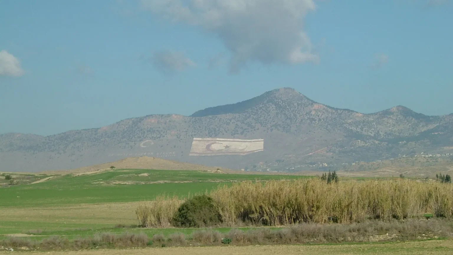 Τεράστιες σημαίες της Τουρκίας και του ψευδοκράτους σχηματισμένες στην πλαγιά του Πενταδάκτυλου, πίσω από πεδιάδα
