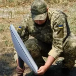 Στρατιώτης με στολή παραλλαγής στήνει δορυφορικό τερματικό Starlink στο έδαφος
