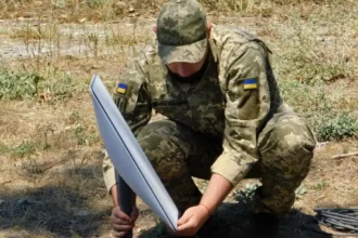 Στρατιώτης με στολή παραλλαγής στήνει δορυφορικό τερματικό Starlink στο έδαφος