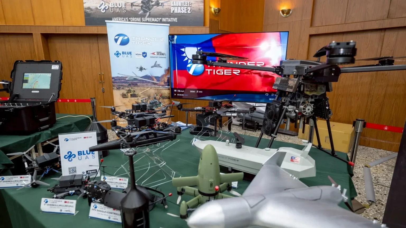 Τραπέζι με διάφορα drones πολλαπλών ελίκων και FPV, οθόνη με τη σημαία της Ταϊβάν και πανό Blue UAS