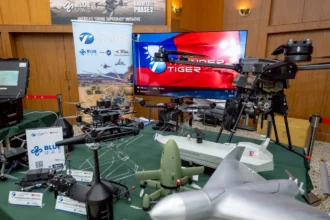 Τραπέζι με διάφορα drones πολλαπλών ελίκων και FPV, οθόνη με τη σημαία της Ταϊβάν και πανό Blue UAS