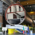 Τμήμα κελύφους υποβρυχίου U212NFS σε υπόστεγο του ναυπηγείου της Fincantieri στο Μουτζιάνο, με την ιταλική και την ευρωπαϊκή σημαία μπροστά του